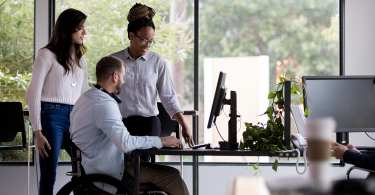 2 Woman 1 man in wheelchair working at desk_1400x800